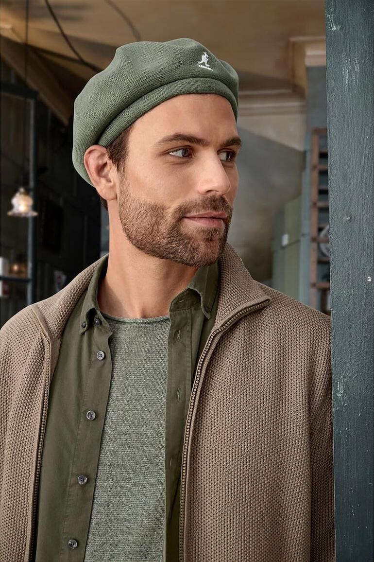 Mann trägt Kangol Bambus-Barett in grünem Farbton, lässig auf einem urbanen Hintergrund.