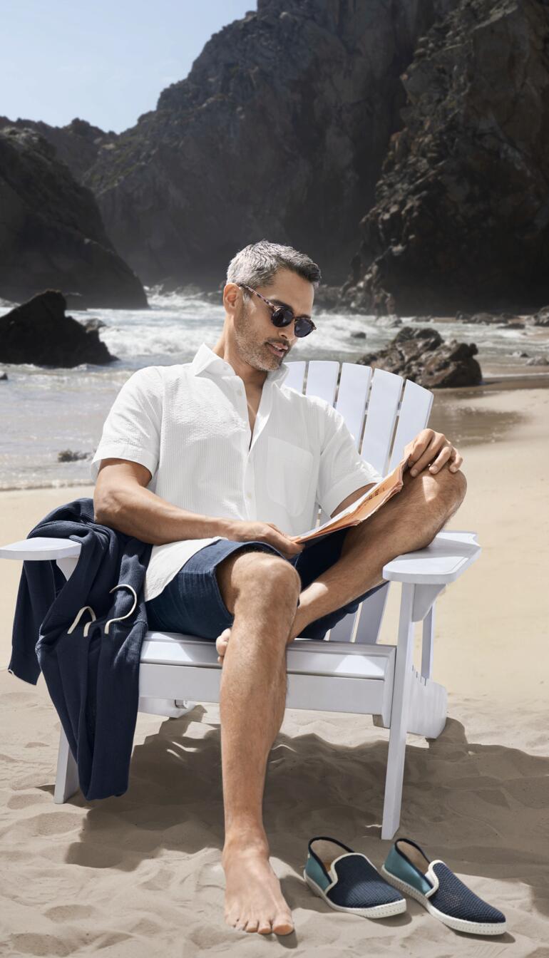 Mann in Seersucker-Hemd sitzt entspannt auf einem Stuhl am Strand.