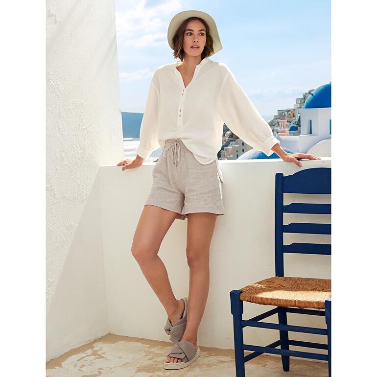 Tunika und Shorts Frau trägt offwhite Tetra-Tunika und kurze Hosen auf einer Terrasse.