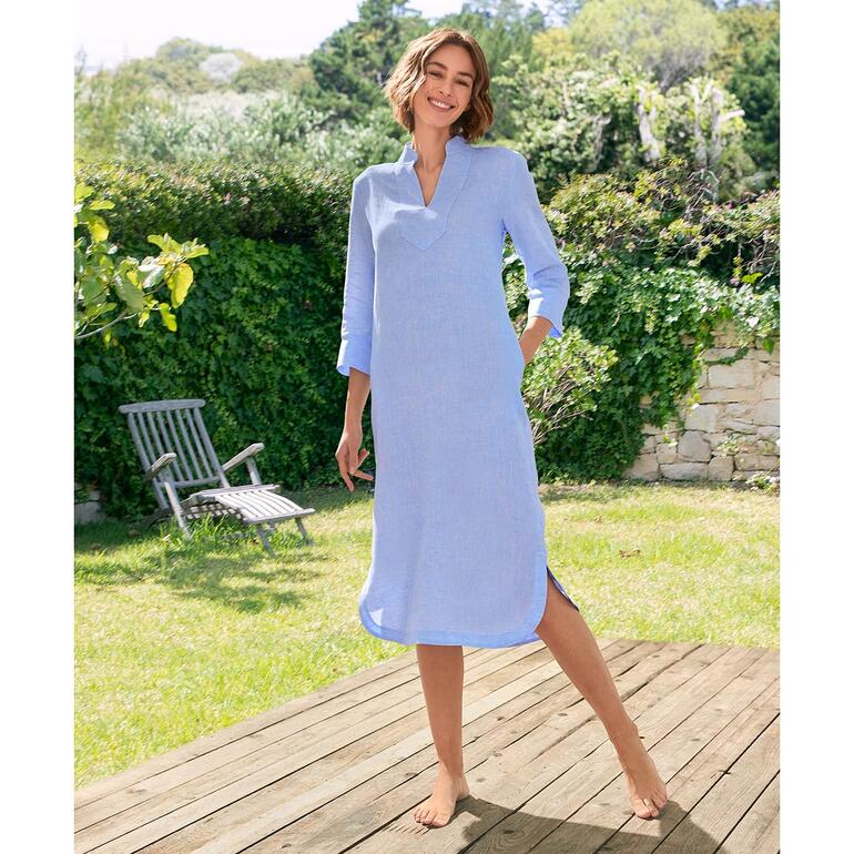 Leinen-Tunika-Kleid Frau in blauem Leinen-Tunika-Kleid, steht im Garten