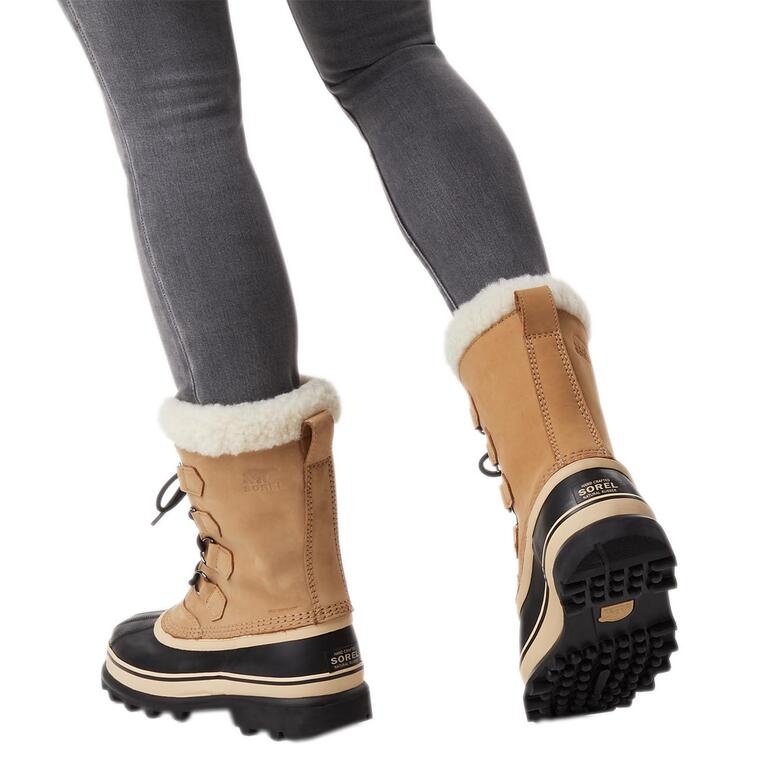 Damen, Camel Frau trägt Sorel Winterboots 'Caribou' in Camel mit schwarzem Unterteil.