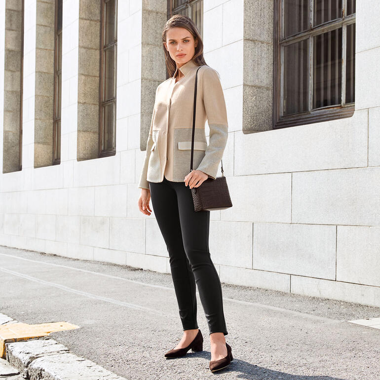 Pourchet Paris Boxy-Bag, Kroko Frau in alpaka-farbigem Blazer mit Tasche, steht gegen eine Wand.