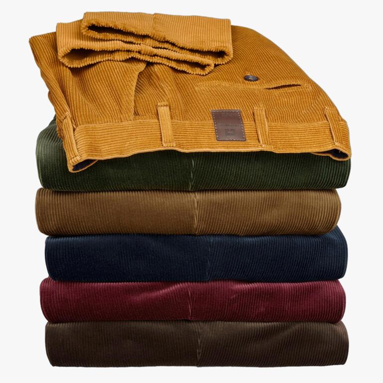Gestapelte Kindermann Cordhosen in verschiedenen Farben, ordentlich aufeinandergelegt.