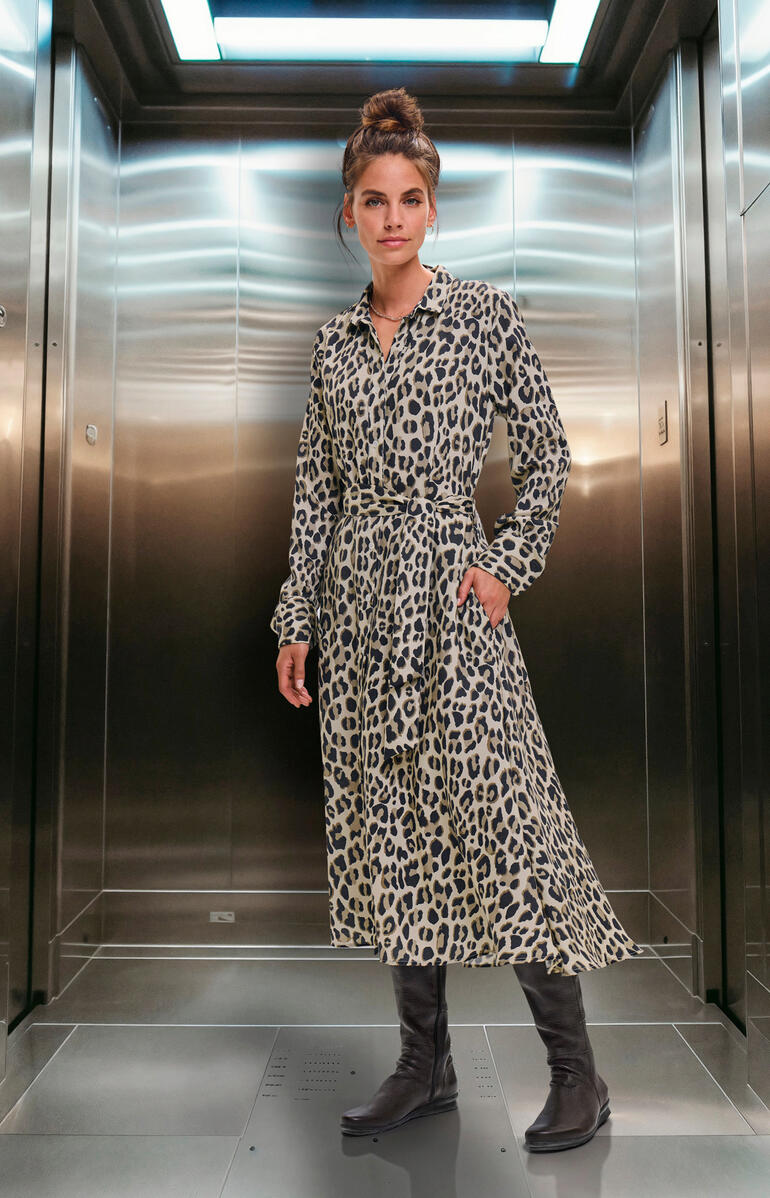 Braun Dame in Leo-Kleid steht in einem Aufzug.