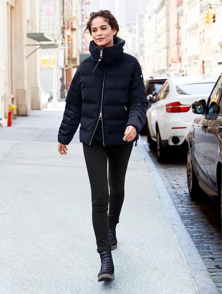 Frau in schwarzer Jacke und Hose mit Schlupf-Boots auf der Straße.