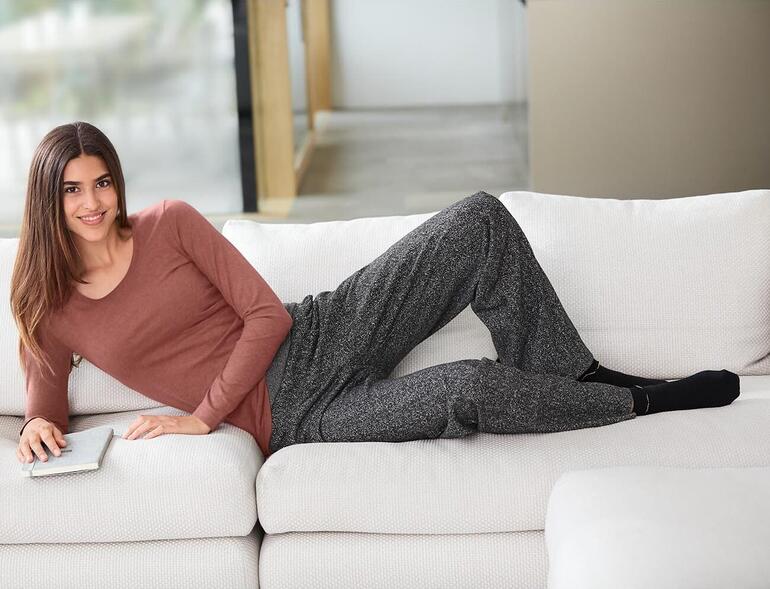Marsala Frau in Braunem Alpaka-Pima-Shirt und grauen Hosen, entspannt auf Sofa.