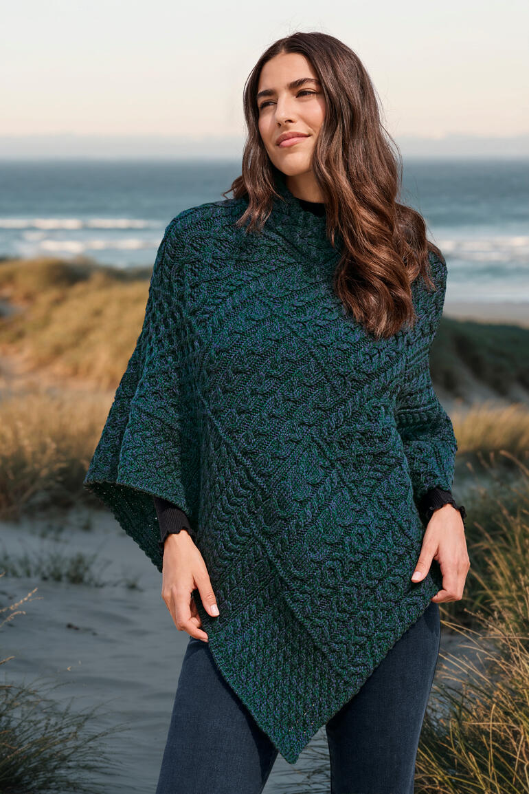 Frau im Aran-Poncho posiert am Strand.