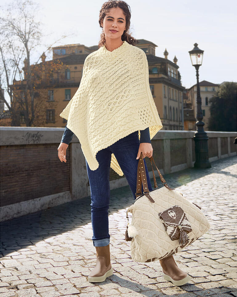 Frau in beigem Pullover-Poncho mit gehäkeltem Muster und Jeans im Freien.