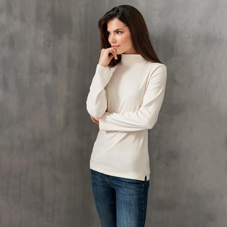 Offwhite Frau in cremefarbenem Baumwoll/Kaschmir-Highneck-Shirt und Jeans.