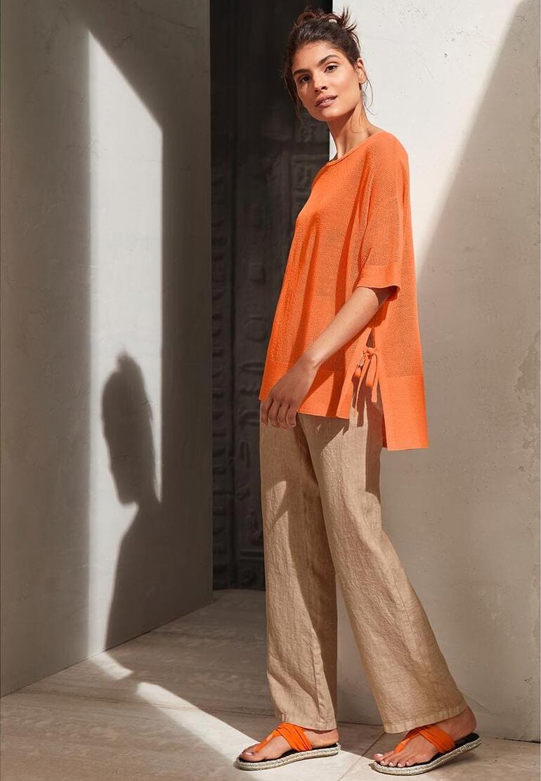 Orange Frau in orangefarbenem Oberteil und Zehensandalen, posed in minimalistischem Raum