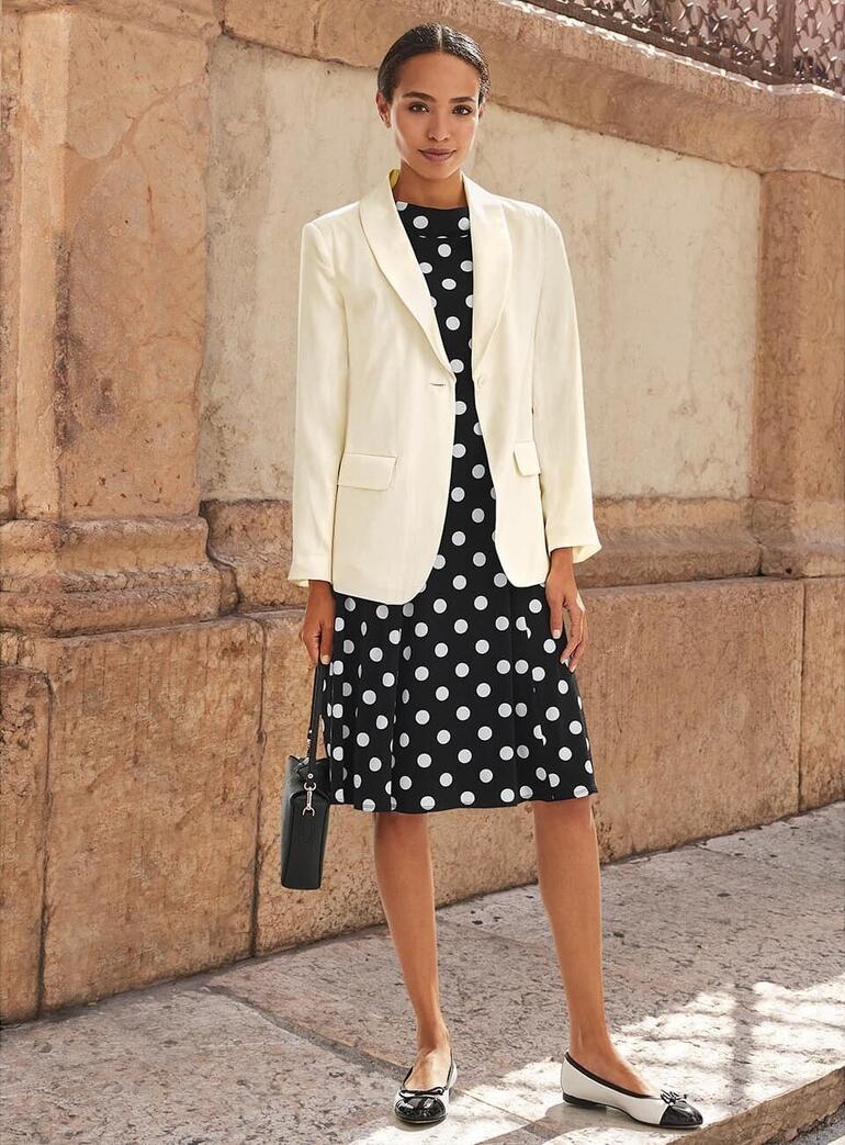 Joyce & Girls Seidenblazer Weißer Seidenblazer über einem schwarzen gepunkteten Kleid.