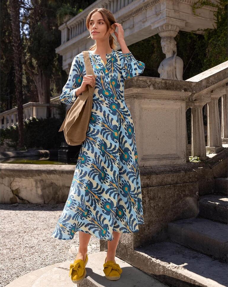 Nimo With Love Ikat-Kleid Frau trägt ein Ikat-Kleid mit buntem Muster, steht auf einer Treppe im Freien.