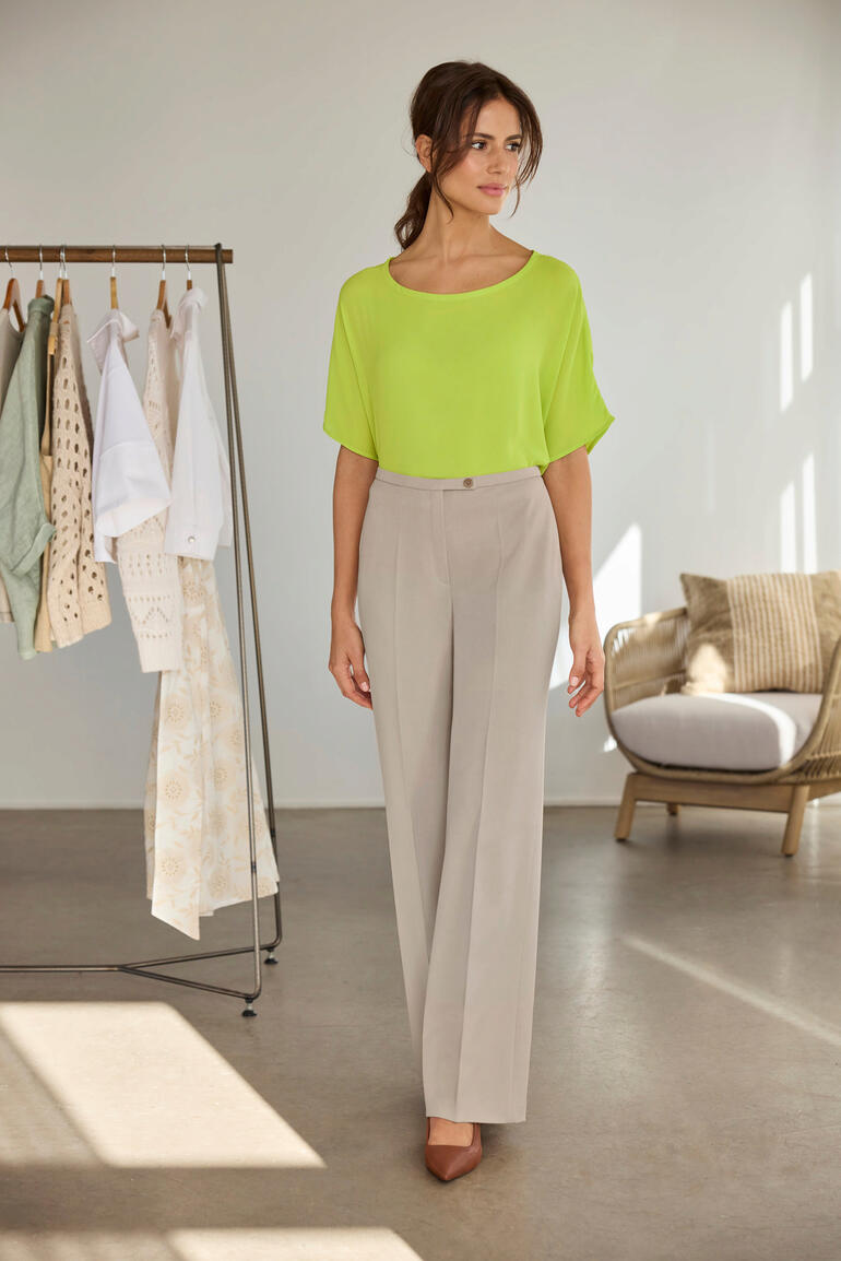 Frau in einer leuchtend gelben T-Shirt-Bluse, neben einem Kleiderständer.