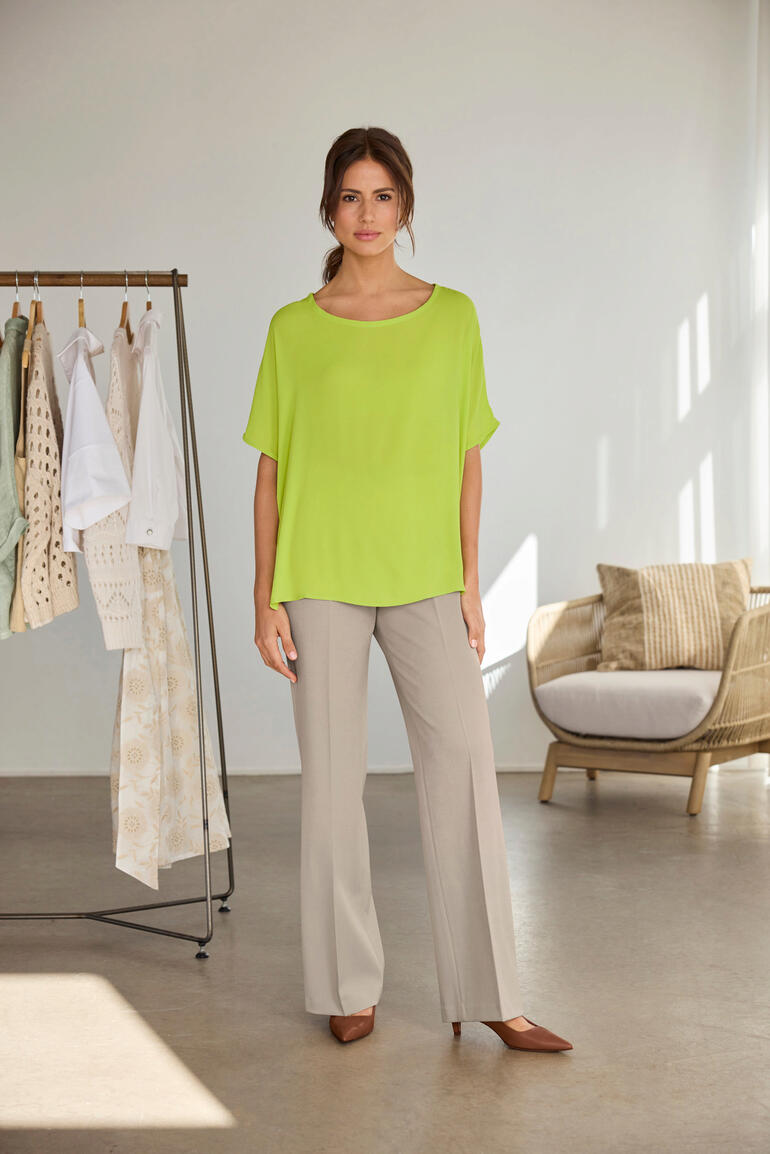 Frau in einer limettengrünen T-Shirt-Bluse, steht lässig neben einem Kleiderständer.