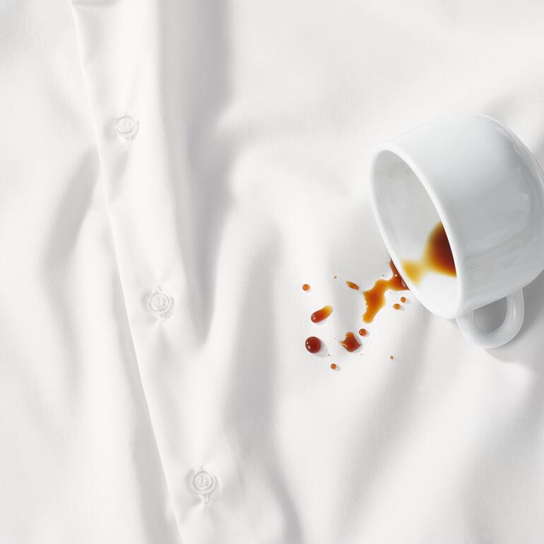 Weißes Hemd mit Kaffeefleck und Tasse daneben.
