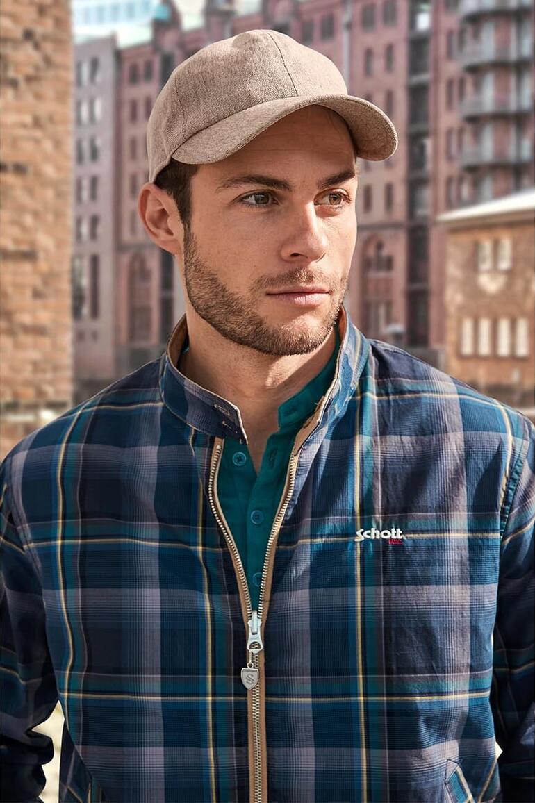 Mann mit Basecap und kariertem Hemd, draußen in einer städtischen Umgebung.