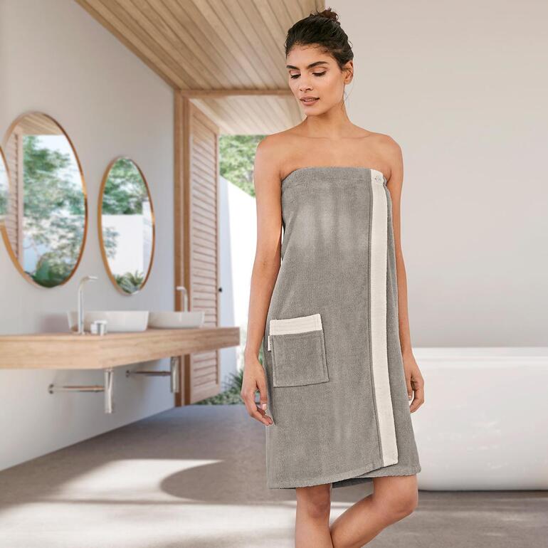 Silbergrau/Offwhite Frau in einem grauen Sauna-Sarong mit seitlicher Tasche in einem modernen Badezimmer.
