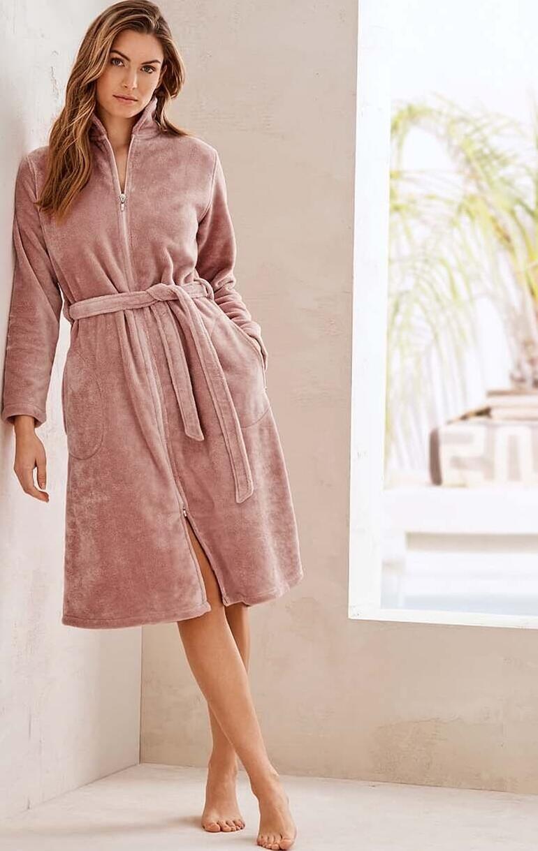 Couture-Bademantel Frau in rosa Couture-Bademantel, stehend an einer Wand.