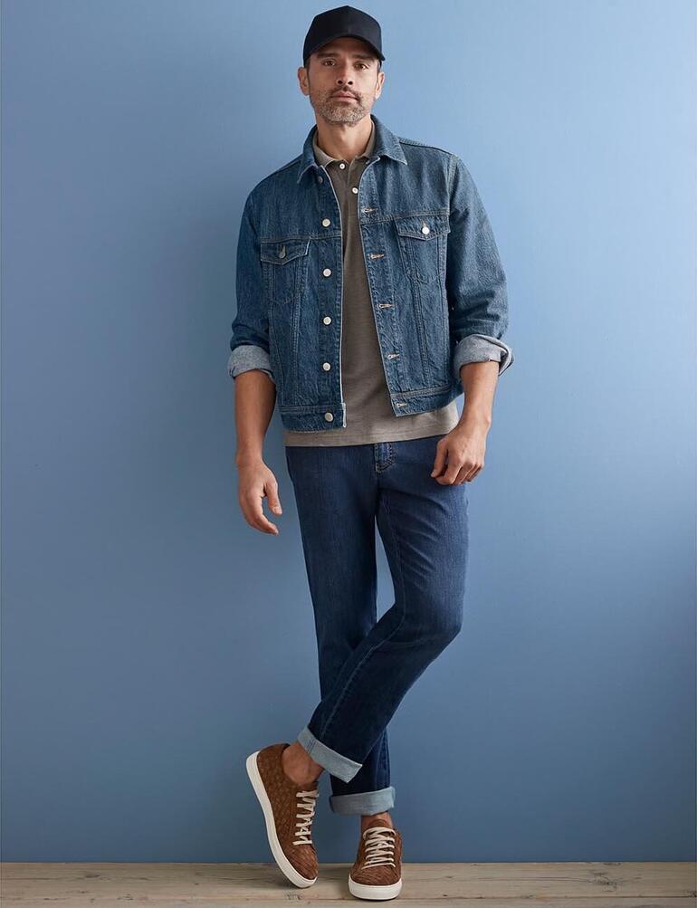 Stetson Trucker-Cap Mann in Hanf-Jeansjacke, lässig vor blauer Wand stehend.