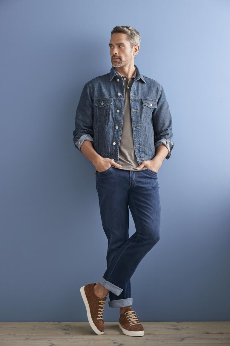 Blau Mann in OCONI Hanf-Jeansjacke vor blauem Hintergrund, mit Jeans und Sneakers.