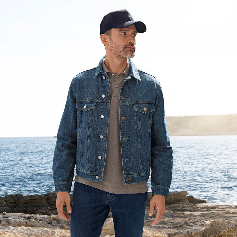 Mann in OCONI Hanf-Jeansjacke steht am Meer mit einem grauen Polohemd.