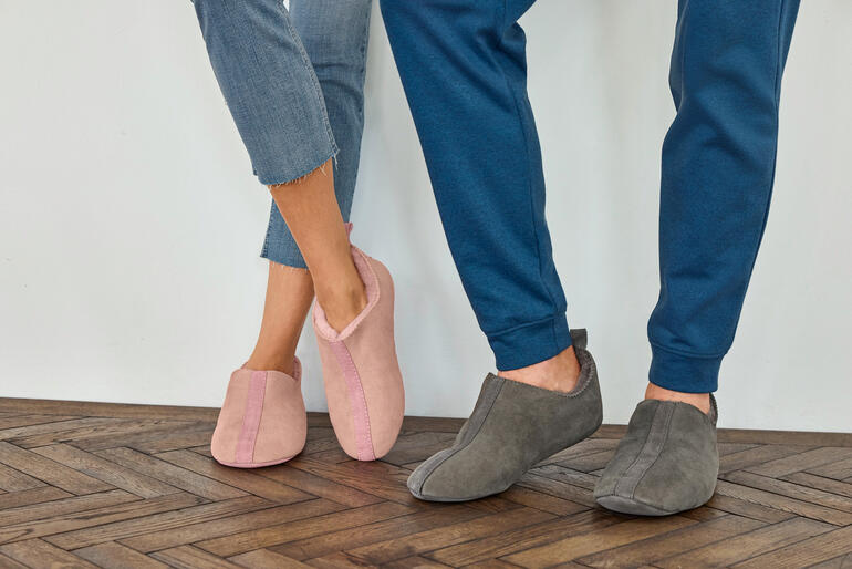 Damen, Rosa und Herren, Grau Paar Lammfell-Slip-ons in rosa und grau auf einem Boden.