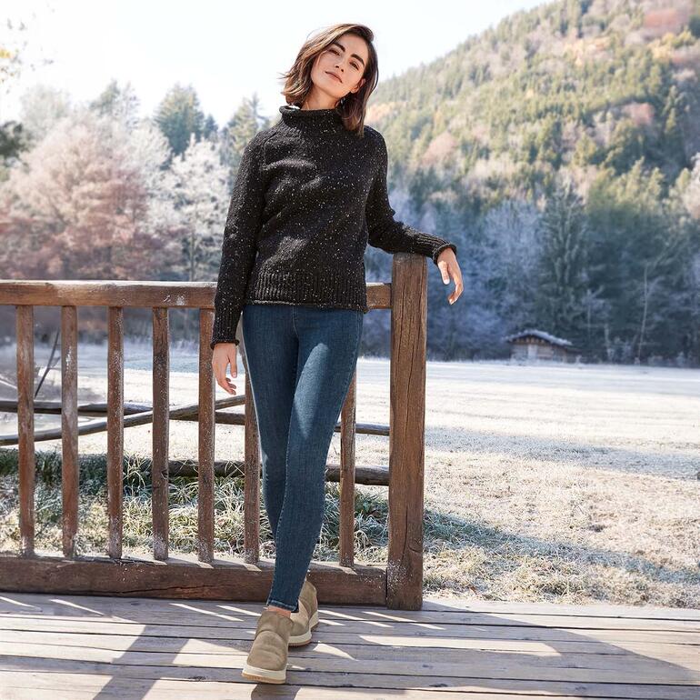 Werner Lammfell-Sneaker Frau in schwarzem Pullover und Jeans im Freien mit verschneiten Bäumen im Hintergrund.