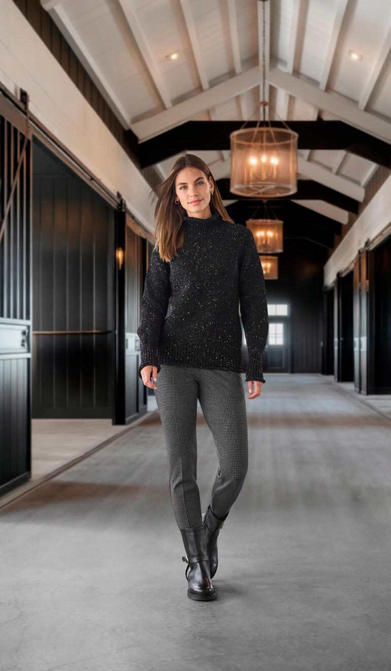 Werner Edel-Bikerboots Frau in schwarzem Pullover und Hahnentritthosen in moderner Halle.