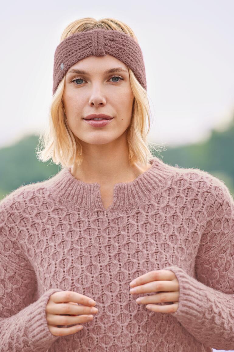 Frau mit Alpaka-Stirnband in Rosa und Grobstrickpullover.