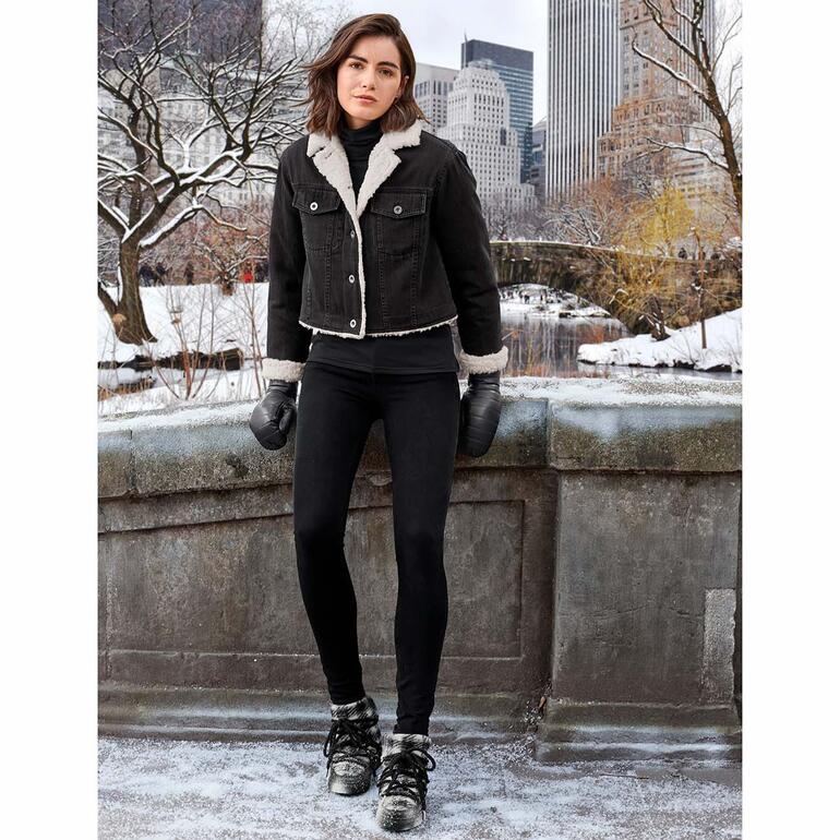Liu Jo Jeans 3D-Shaping-Jeans Frau in 3D shaping-Jeans mit schwarzer Jacke und warmen Handschuhen in einer winterlichen Stadtlandschaft.