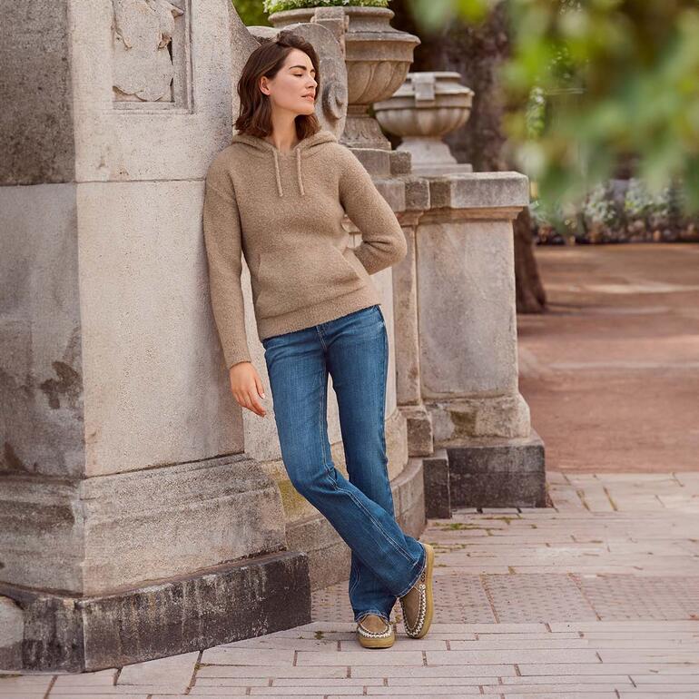 laidback london Boho-Mokassin Frau in Kamelhaar-Hoodie lehnt gegen eine Säule im Freien