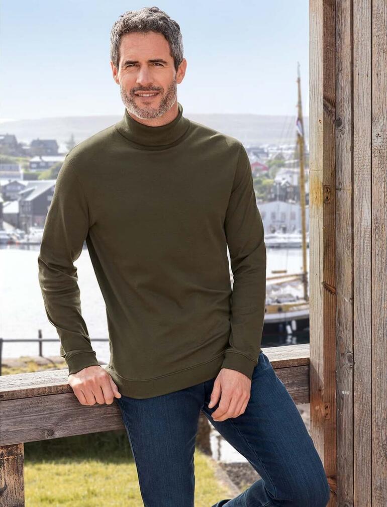 Herren, Oliv Mann trägt olivgrünen Rollkragenpullover vor einer Hafenlandschaft.
