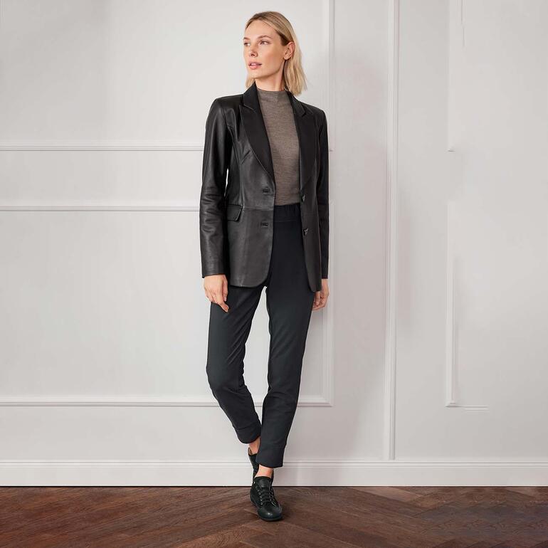 OCONI Olivengegerbter Lammnappa-Blazer Dame trägt schwarzen Stretch-Rolli mit Anzughose in elegantem Ambiente.