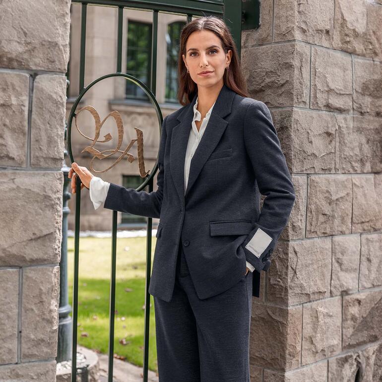 Blazer und Hose Porträt einer Frau in einem schwarzen Blazer, der an einer Säule lehnt.