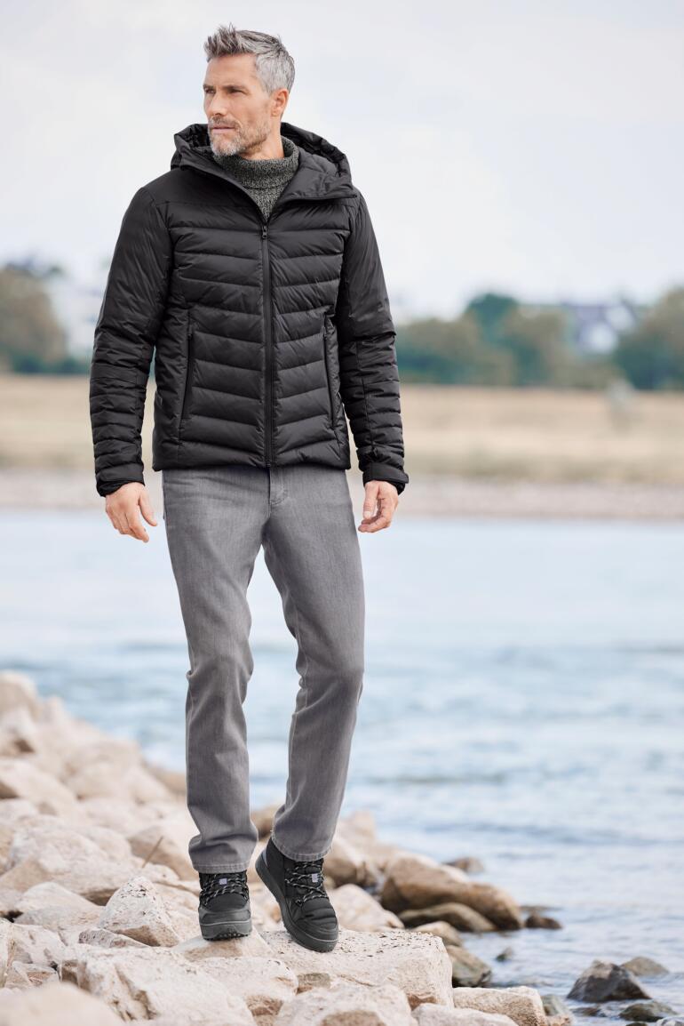 Daunen-Regenjacke Mann in Daunen-Regenjacke, steht am Wasser und lächelt.