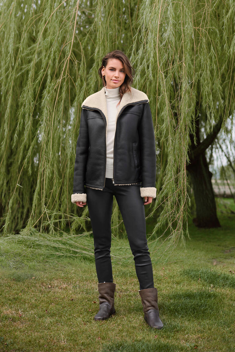 OCONI Curlylamm-Fliegerjacke Frau in einer schwarzen OCONI Curlylamm-Fliegerjacke, im Freien.