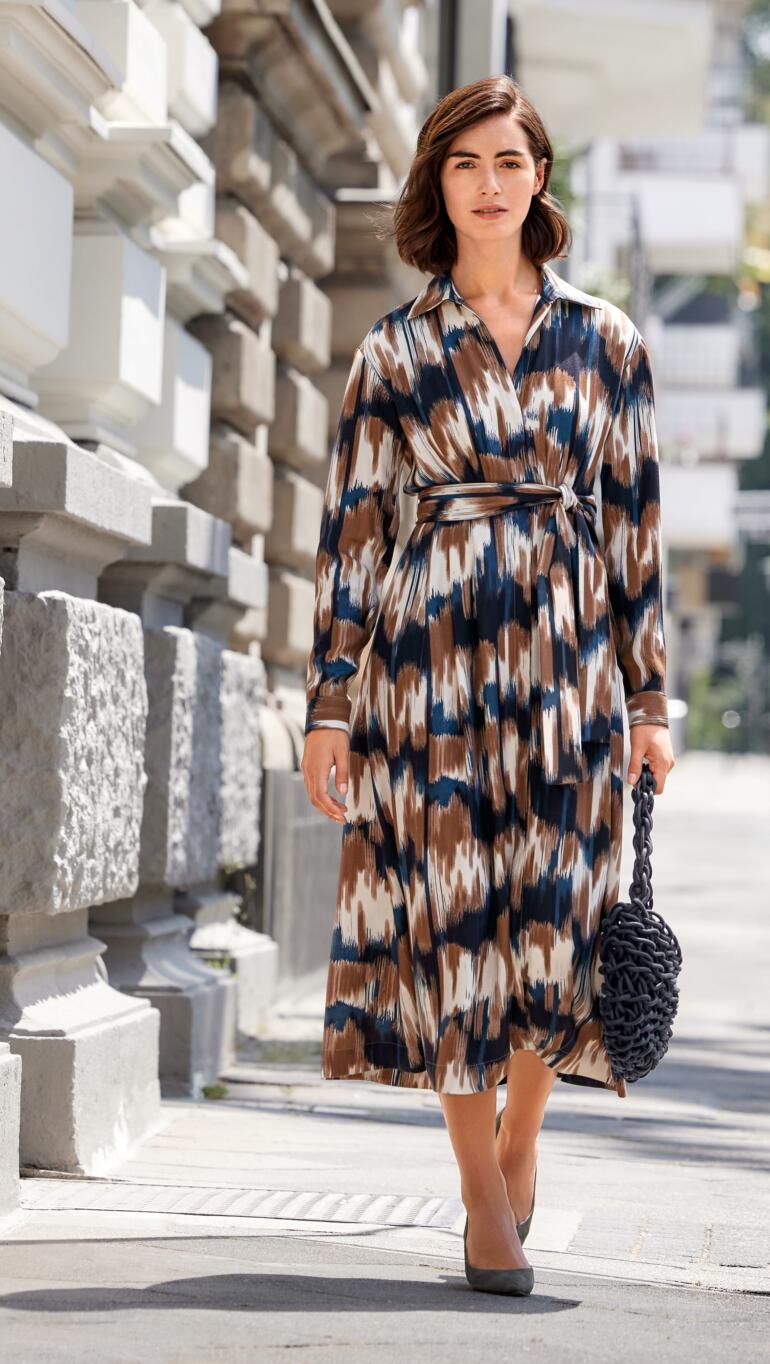 Dame in figurschmeichelndem Kleid mit buntem Muster und Riemen auf der Straße.