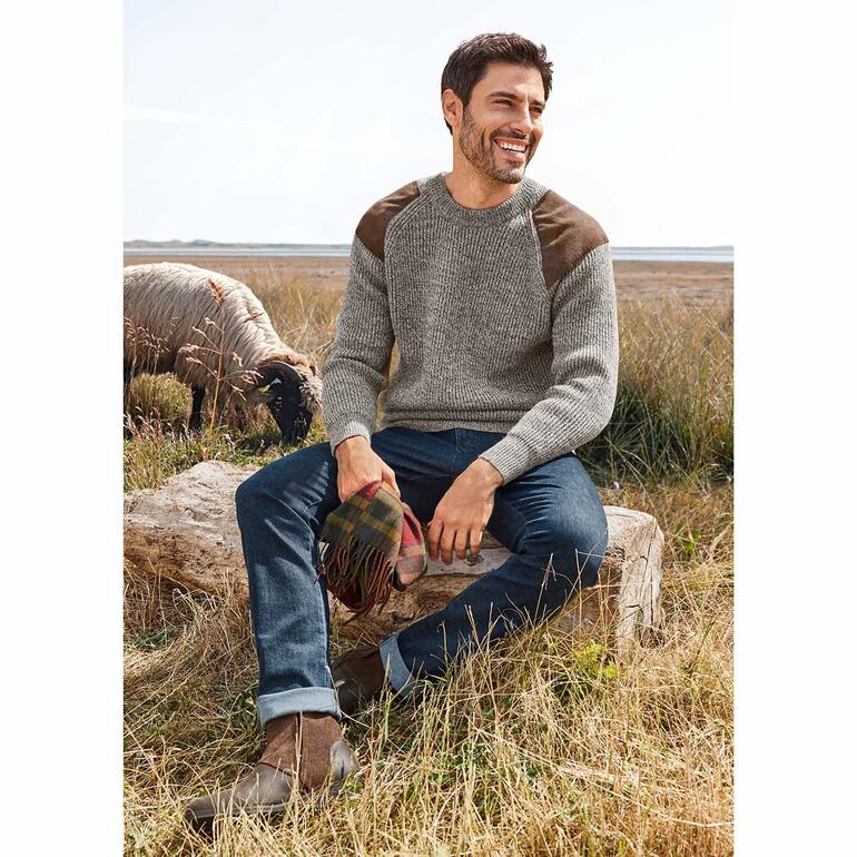Bequeme Kaschmirjeans Mann sitzt auf einem Baumstamm in der Natur, trägt einen grauen Pullover.