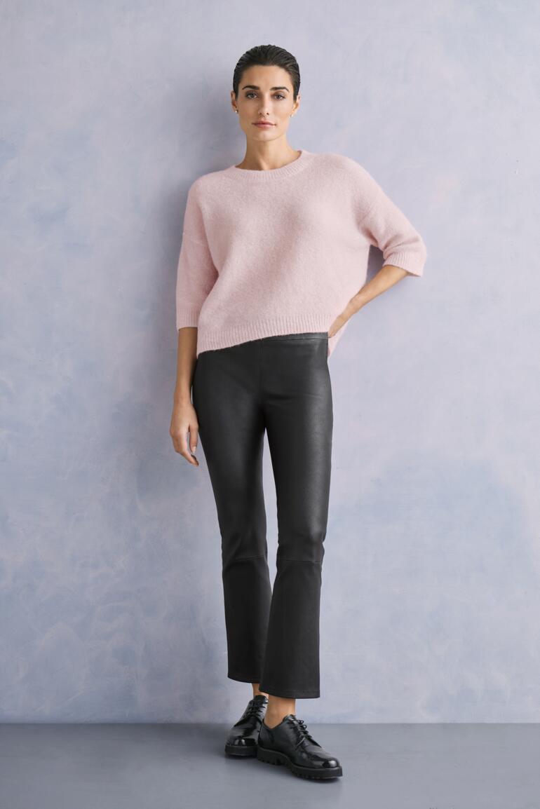 Rosé Frau in pinkem Sweater und schwarzer Kick-Flare-Lederhose vor grauem Hintergrund.