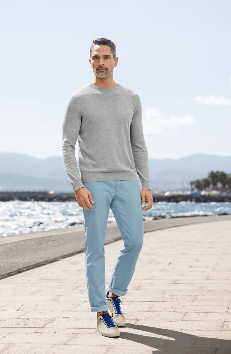 Hellblau Mann in grauem Sommer-Tweed-Pullover und blauen Hosen am Strand.