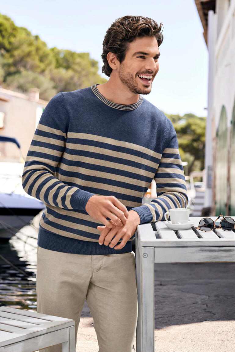 Mann in gestreiftem Pullover steht am Wasser.