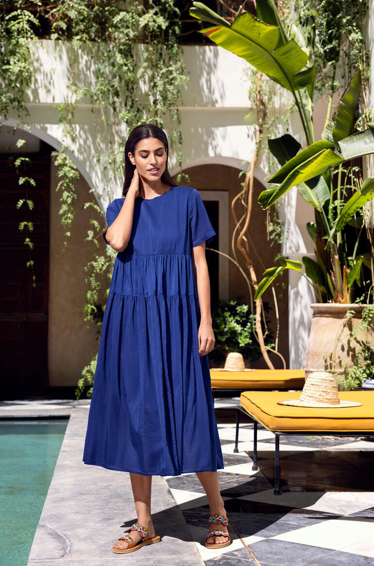 Kiltie Voile-Sommerkleid Frau in blauem Sommerkleid steht vor einer eleganten Kulisse