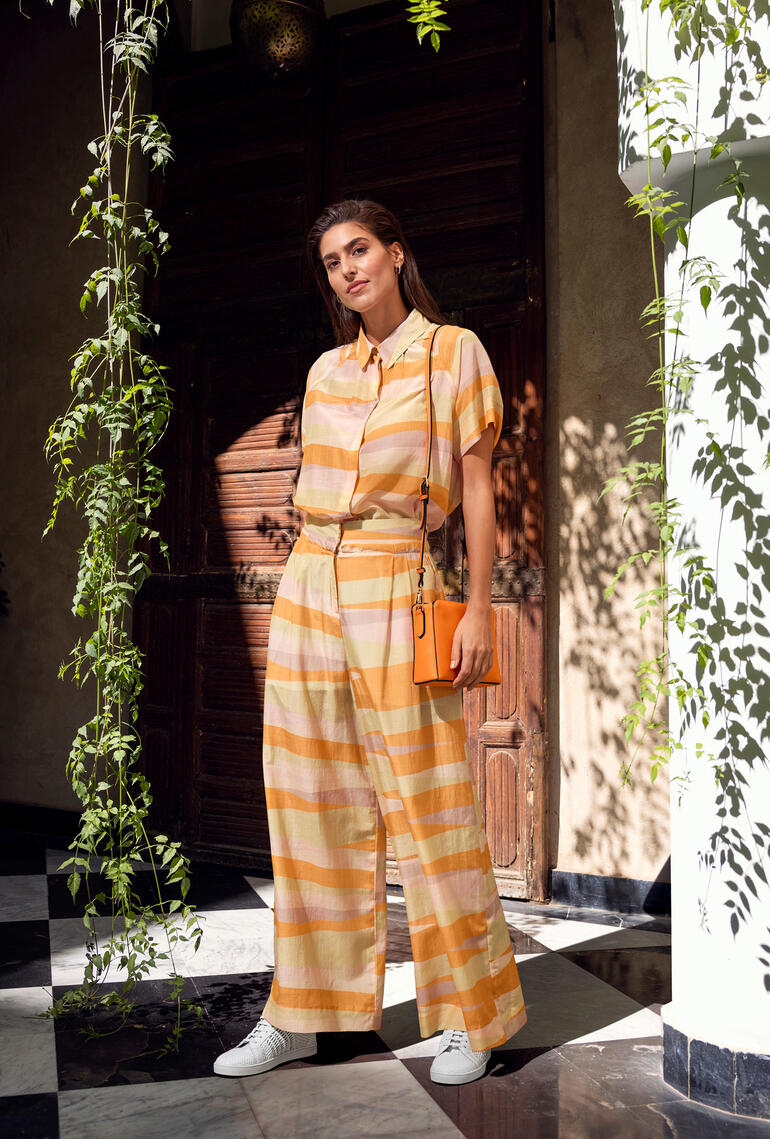 Frau im gestreiften Color-Batist-Zweiteiler steht in einem Raum mit Pflanzen.