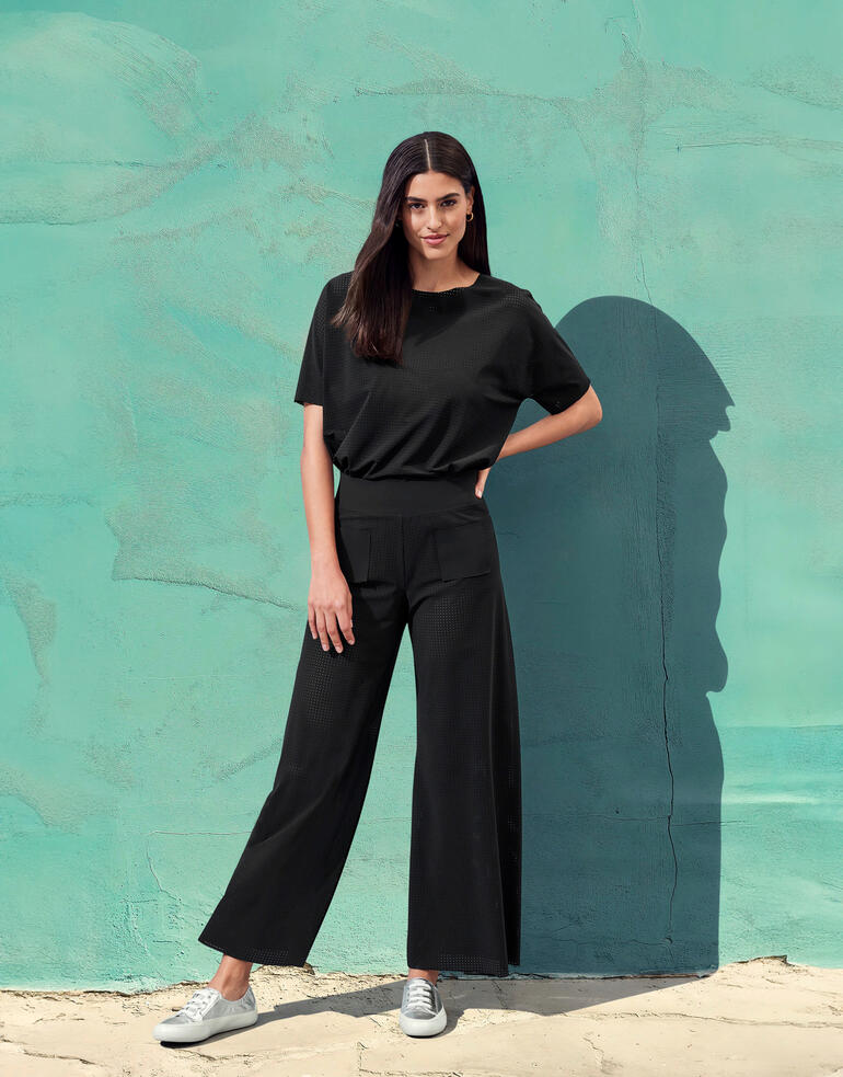 Frau trägt schwarze Hightech-Jersey-Kombi mit grauer Wand im Hintergrund