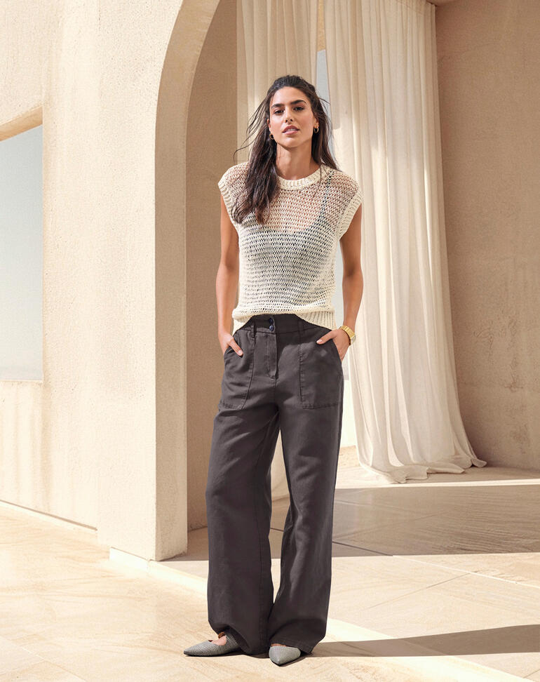 Frau in Spitzen-Oberteil und weiten Hosen, stehend in einem hellen Raum.