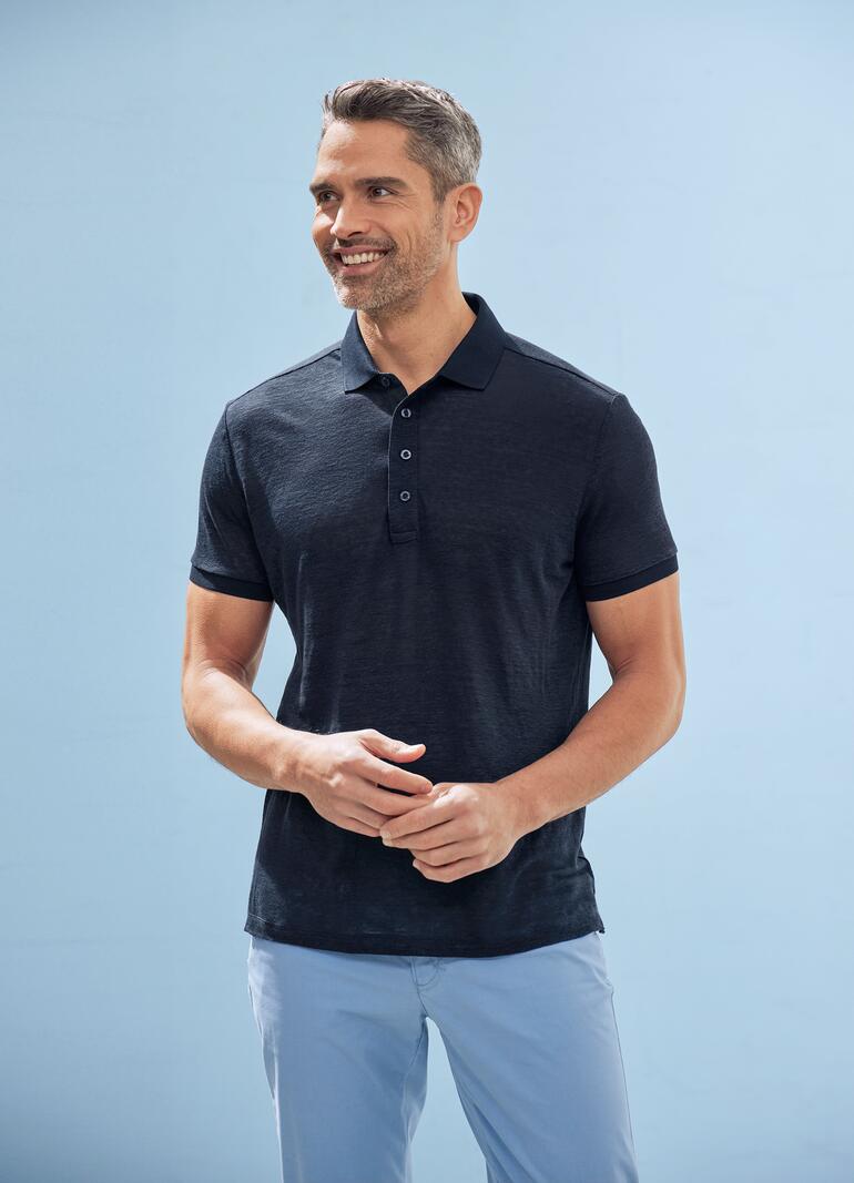 Blau Schwarz gekleideter Mann mit dunkelgrau-blauem Polo auf blauem Hintergrund.