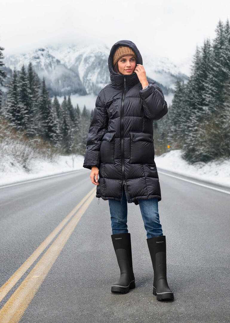 Frau in Taion Daunen-Parka mit Kapuze stehend in winterlicher Landschaft.