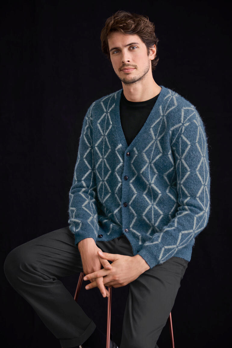 Brushed-Alpaka-Cardigan Mann sitzt in einem blauen Brushed-Alpaka-Cardigan mit Rautenmuster.