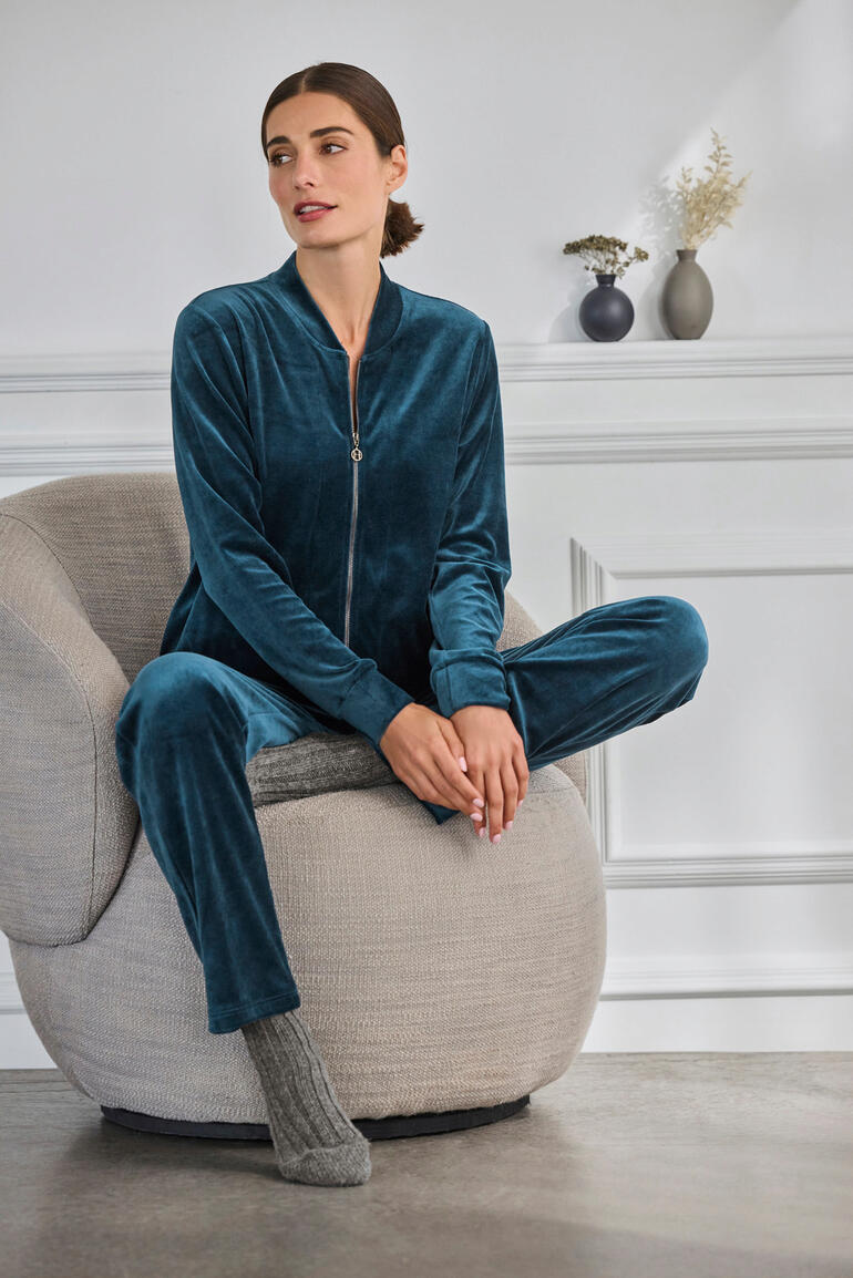 Hanro Loungewear-Samt-Anzug Frau sitzt in einem bequemen Sessel, trägt Hanro Loungewear-Samt-Anzug in Grün.