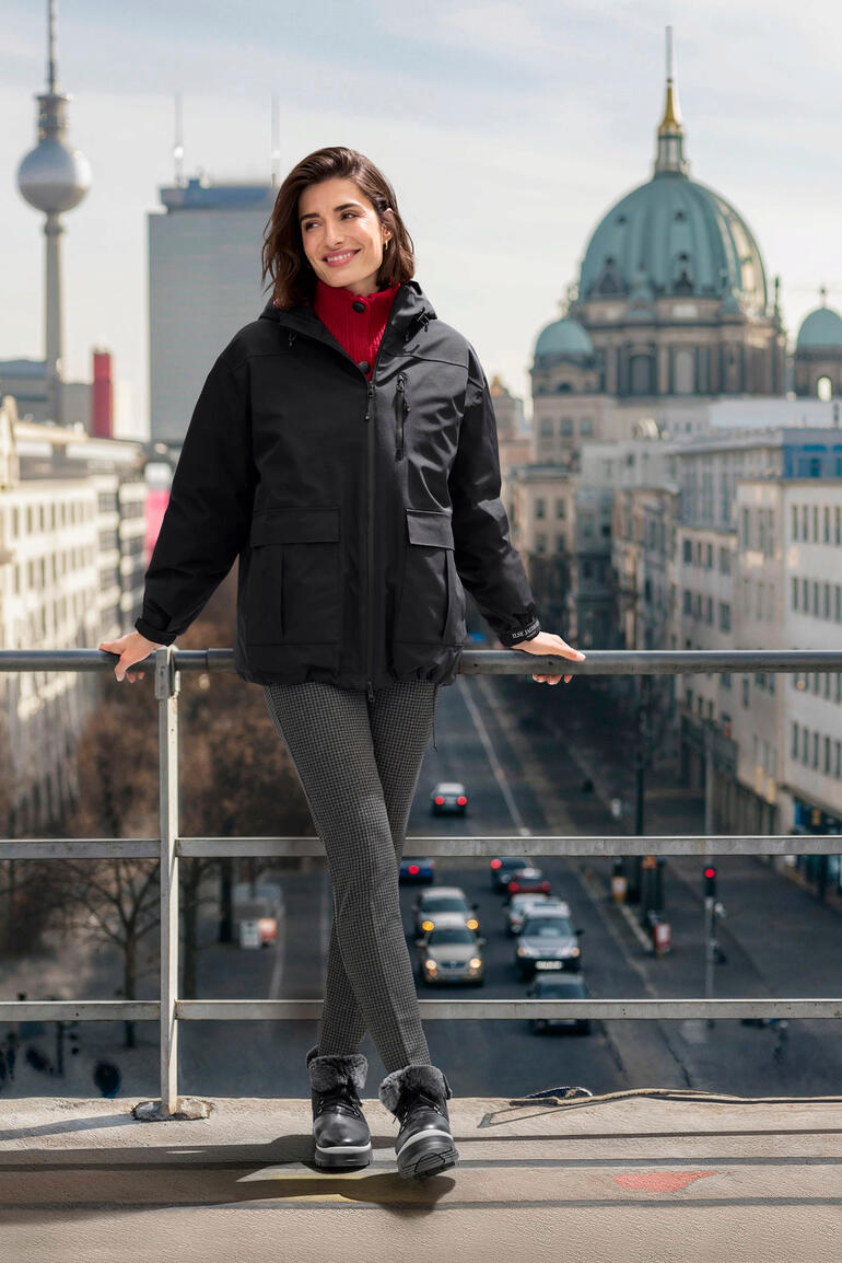 Schwarz Frau in schwarzer Daunen-Regenjacke vor städtischer Kulisse.